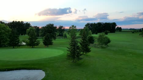 Vuelo-Pacífico-De-Drones-Al-Atardecer-En-El-Campo-De-Golf-Para-Poner-Verde-Con-Bandera-Roja