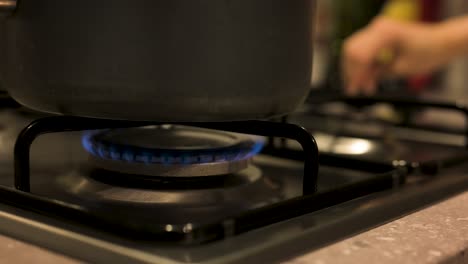 Turning-gas-stove-down-with-pot-on-top-close-up,-slow-motion