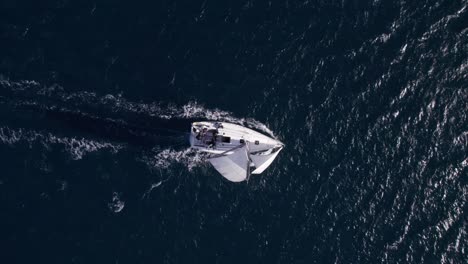 Yate-De-Vela-Moviéndose-Por-El-Viento-En-Aguas-Azules-Tranquilas-En-Un-Día-Soleado,-De-Arriba-Hacia-Abajo