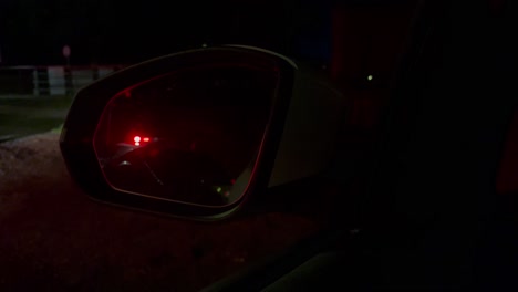Police-lights-flashing-in-back-or-wing-mirror-of-car,-night-closeup-view-of-beacon-reflection