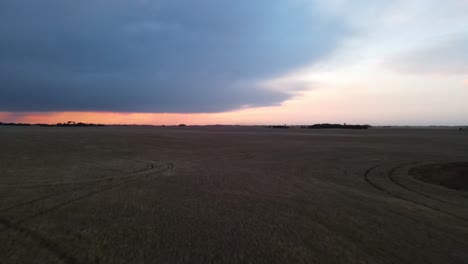 Curved-drone-flight-over-flat,-expansive-farm-land-revealing-a-dramatic,-cloudy-sunset-in-Alberta,-Canada