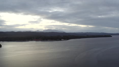 Aerial:-Drone-flying-over-a-large-lake-towards-the-mountains-on-the-horizon-near-Strahan,-Australia