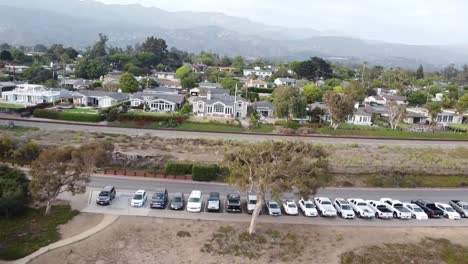 Drone-flies-out-from-housing-track-with-parking-lot-along-train-track-to-sea-shore