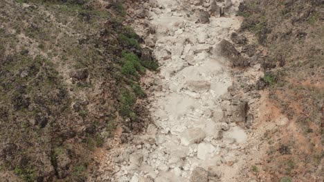 Dry-riverbed-in-the-wilderness,-with-large-boulders-invaded