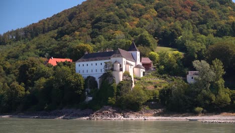 Slow-motion-view-of-castle-next-to-river-as-seen-from-Danube-cruise-in-Wachau,-Austria