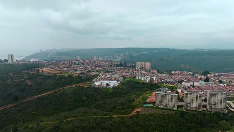 Wide-Aerial-view-of-Achupallas-neighborhood-on-a-forested-hilltop-on-Cloudy-day,-Chile
