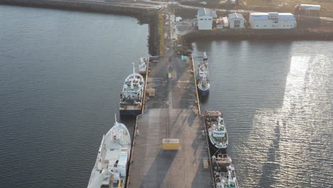 SandgerÃ°i-fishing-boats-anchored-at-dock-during-bright-sunrise,-aerial