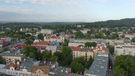 Aerial-drone-forward-moving-shot-over-residential-buildings-in-Krakow,-Cracow-in-Poland-along-hilly-terrain-in-the-background