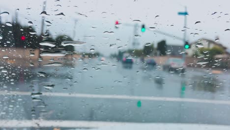 Raindrops-on-windshield-at-traffic-lights,-closeup
