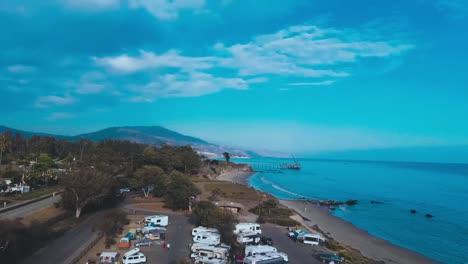 Drone-fly-over-RV-park-with-ocean-and-mountain-in-the-background