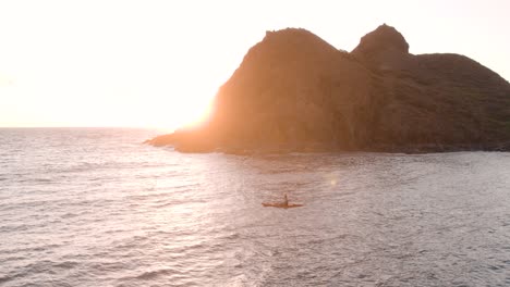 Man-paddles-aboard-red-kayak-near-Na-Mokulua-Hawaiian-islands-with-sunset-in-background