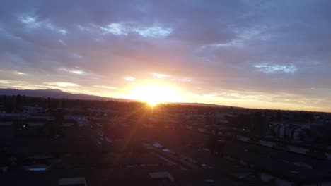 Sunrise-through-clouds-over-cityscape,-drone-shot