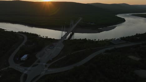 Aerial-view-over-the-Utsjoki-town,-towards-the-Sami-Bridge-and-Teno-river,-midnight-sun-in-Utsjoki,-Finland---rising,-tilt,-drone-shot