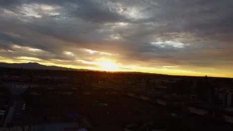 Drone-shot-pulling-back-over-city-with-sunrise-in-clouds,-wide-shot