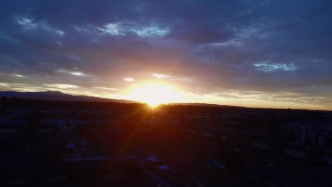 Sun-rays-through-clouds-over-cityscape,-drone-shot-1