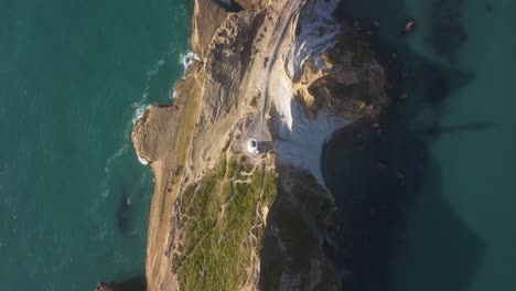 Directly-above-Castlepoint-lighthouse-in-New-Zealand,-moving-along-the-ridgeline-of-a-cliff-towards-a-rocky-bay-and-beach