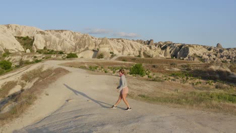 Female-in-pink-running-up-hill-and-jumping-for-you-between-fairy-chimney-rock-formations-in-cappadocial-turkey-landscape