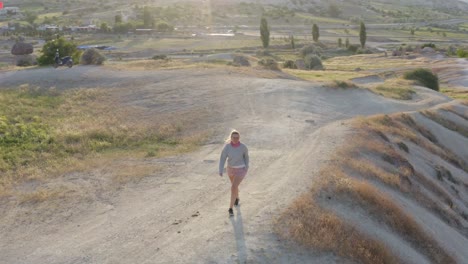 Mujer-Rubia-En-Rosa-Corriendo-Por-La-Colina-En-Capadocia-Turquía-Entre-Formaciones-De-Chimeneas-De-Cuento-De-Hadas-En-Una-Aventura