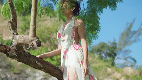 Low-angle-view-of-a-red-hair-latina-standing-on-a-tree-trunk-in-a-long-flower-dress-at-a-park