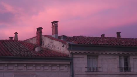 Fiery-pink-sunset-over-building-chimneys-and-tiled-roof-with-copy-space