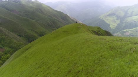 DRONE-LOW-RISE-green-mountains-APPROACH-BEHIND-group-of-people-on-top-enjoy-the-views