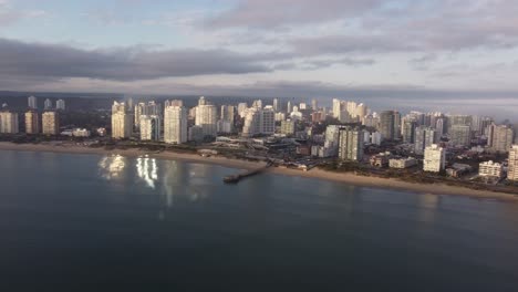 Aerial-approaching-shot-of-beautiful-cityscape-of-Punta-del-Este-with-high-rise-buildings,-beach-and-Atlantic-Ocean-during-golden-hour