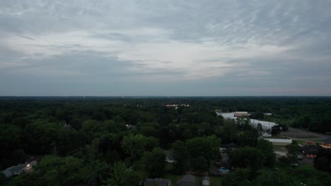 Aerial-drone-shot-over-small-town-surrounded-by-dense-vegetation-during-evening-time