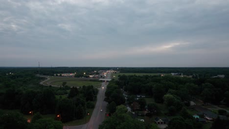 Aerial-drone-forward-moving-shot-over-highway-running-through-small-town-with-cars-passing-by-during-evening-time