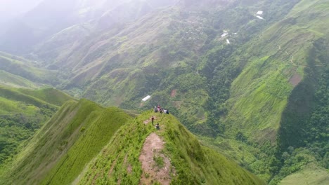 Stunning-aerial-view-with-three-mountain-tops-aligned-with-people-from-behind-on-top-cliff