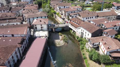 Tilt-down-aerial-shot-over-a-bridge-on-the-Bidasoa-River-in-Elizondo,-capital-of-Baztan-Valley,-with-people-enjoying-the-day