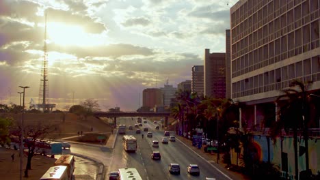Sunbeams-glow-through-the-clouds-as-along-a-busy-street-in-Brasilia,-Brazil---slow-motion