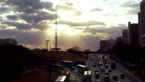 Vehicular-traffic-at-sunset-in-Brasilia,-Brazil-with-sunbeams-streaming-through-a-break-in-the-clouds---slow-motion