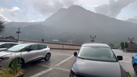 Wide-shot-of-rain-and-hail-hitting-a-car-during-the-day-in-the-street-of-gavarnie-gedre-village-in-the-wild-pyrenees-mountain-national-parc