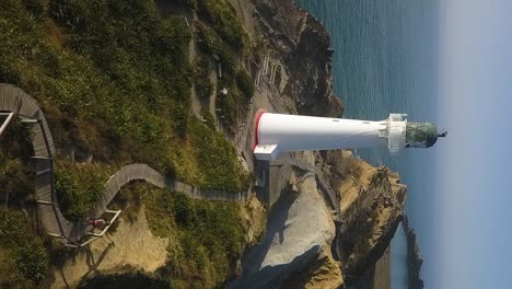 An-active-blonde-woman-runs-along-a-pathway-towards-a-white-lighthouse-on-a-sunny-day