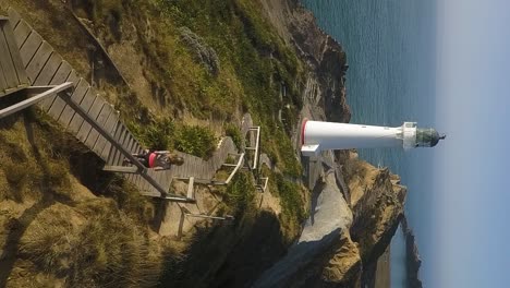 A-woman-jogs-down-a-wooden-boardwalk-toward-a-white-lighthouse-in-New-Zealand