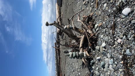 Driftwood-En-Una-Orilla-Rocosa-Con-Mojones-De-Piedra-Equilibrados-En-Las-Ramas---Orientación-Vertical