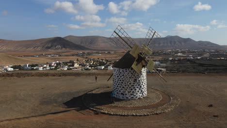 Aerial-shot-in-orbit-over-an-old-grain-mill-in-Fuerteventura,-visualizing-the-mountains-around-Villaverde