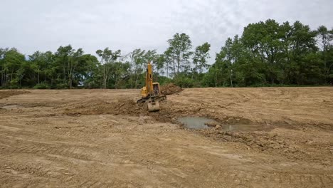 Hydraulic-excavator-digging-dirt-from-bottom-of-pond-and-moving-it-to-top-of-side-wall-of-pond-at-a-land-development-site