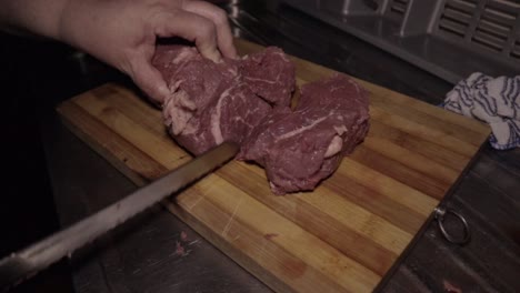 Female-Hands-Cutting-a-Big-Piece-of-Meat-with-a-Serrated-Knife-on-a-Wooden-Chopping-Board