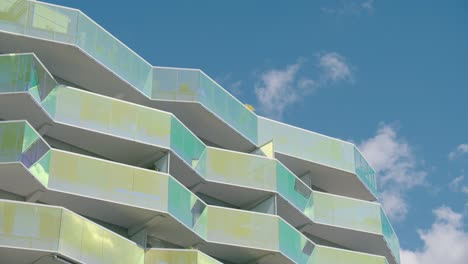 Modern-building-with-glass-balconies,-pan-left-against-sky-and-clouds