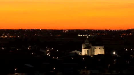 Aerial-spotlight-of-building-illuminated-at-night-with-orange-sky-at-sunset