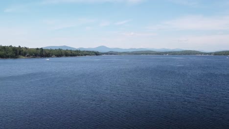 Aerial-drone-shot-over-Lovewell-Pond-in-Maine,-with-mountain-range-in-distance-and-kayakers-on-a-sand-bar