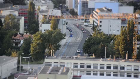 Timelapse-with-miniature-effect-of-a-street-in-a-small-city-with-cars-driving-and-stopping-at-a-cross-section-with-houses-and-a-crane-around