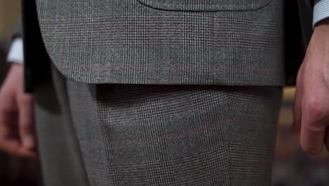 Wearing-tweed-suit-and-feeling-jacket-hem-with-thumb,-close-up