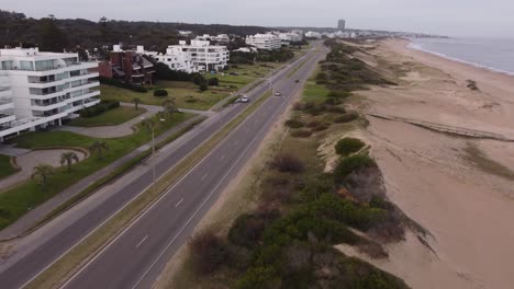 Aerial-tracking-shot-of-four-wheel-vehicle-driving-on-boulevard-avenue-along-coastline-of-Punta-del-Este,Uruguay