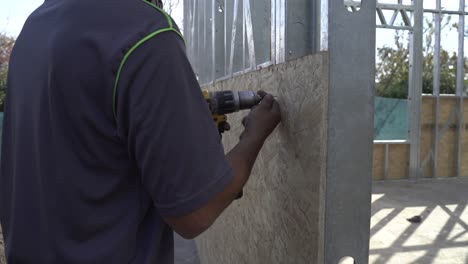 Construction-worker-screws-plywood-to-metal-frame-with-drill