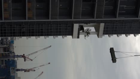Vertical-video---Cranes-on-construction-site,-lifting-heavy-load