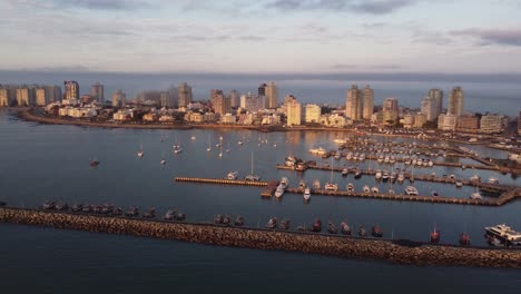 Luftdrohnen-Panoramaaufnahme-Von-Wunderschönen-Beleuchteten-Stadtgebäuden-Und-Dem-Hafen-Der-Stadt-Punta-Del-Este-In-Uruguay-Während-Des-Sonnenuntergangs