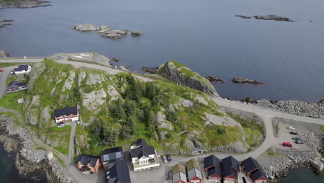 Aerial-panning-up-reveal-shot-of-a-quaint-village-on-the-rocky-island-on-the-coast-with-cliffs-and-mountains-in-the-background-on-an-overcast-day