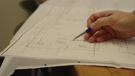 Person-hand-review-and-circling-building-blueprints-with-pen,-close-up-handheld
